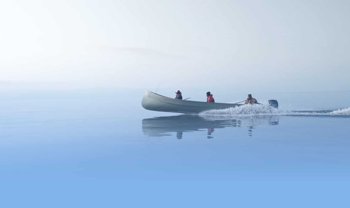 A serene scene of a small motorboat with three people gliding over calm, misty blue water. The horizon blends softly into the sky, creating a tranquil atmosphere.